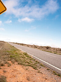 Eine Landstra&szlig;e in Australien. Im Vordergrund steht ein gelbes Schild mit einem K&auml;nguru darauf.