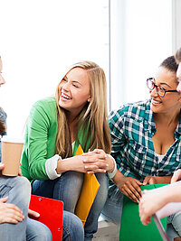 Drei junge Frauen und zwei junge M&auml;nner sitzen gemeinsam auf einer Sitzecke und unterhalten sich lachend miteinander